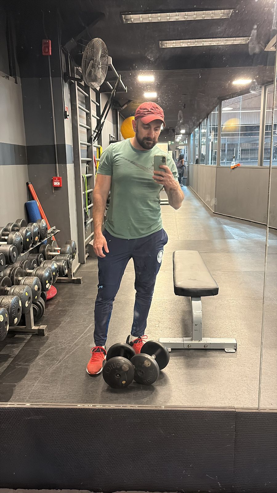 Bruno in the gym where he coaches in São Paulo, in a cap and training clothes, beside a rack of dumbbells.